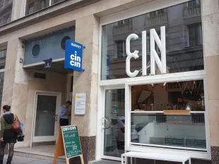 Außenansicht:Restaurants "cin cin" mit Buffet-Schild, Glas-Eingang, Speisekarte mit Pizza und Focaccia. Zwei Personen vor dem Eingang.