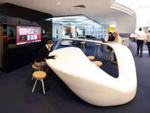 Geschwungene, weiße Theke als zentraler Tisch, umgeben von Hockern, in einem modernen Arbeitsbereich