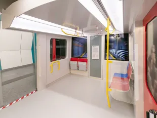 Innenraum des X-Waggons mit weißen Wänden, gelben Haltegriffen und Sitzen in Rot, Blau und Weiß