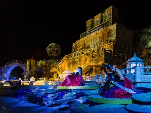 Szene: Zwei Figuren in roten Gewändern auf Seerosenblättern, eine Brücke und ein prächtiges Gebäude 