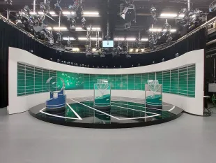 moderne Plattform mit glänzender Lotterie-Maschine und Kugeln, beleuchtet von blauen und weißen Lichtern, umgeben von Kameras und einer digitalen Anzeige.