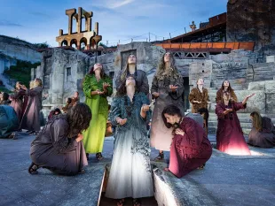 Szene: Gruppe von Darstellern in farbigen Gewändern betet im Steinbruch St. Margarethen, vor einer Kulisse mit goldenem Tempel und steinernen Strukturen