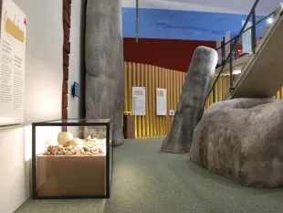 Ausstellungsraum:Vitrine voller Steine, großen künstlichen Felsformationen, Informationsschildern und einer Treppe im Hintergrund