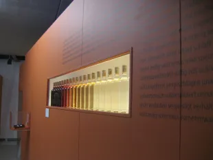 Reihe von Flaschen in verschiedenen Farben hinter beleuchtetem Glas und Texten an der Wand