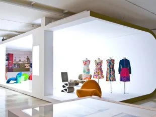 Moderne Ausstellung im Sixties-Stil mit bunter Kleidungskollektion auf Schaufensterpuppen und Stühlen