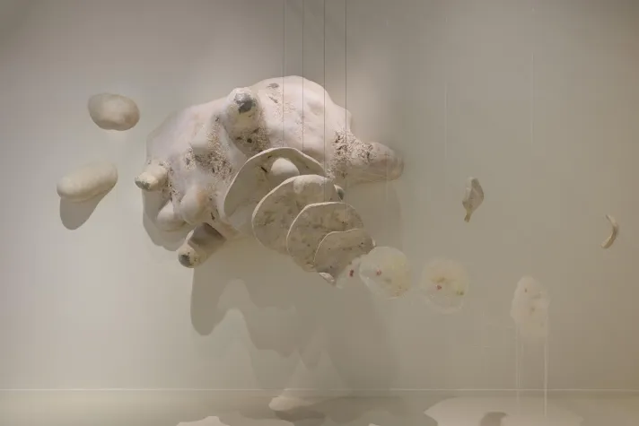 Überlebensgroße Amöbenskulptur und transparente menschliche Fragmente hängen in einem Raum