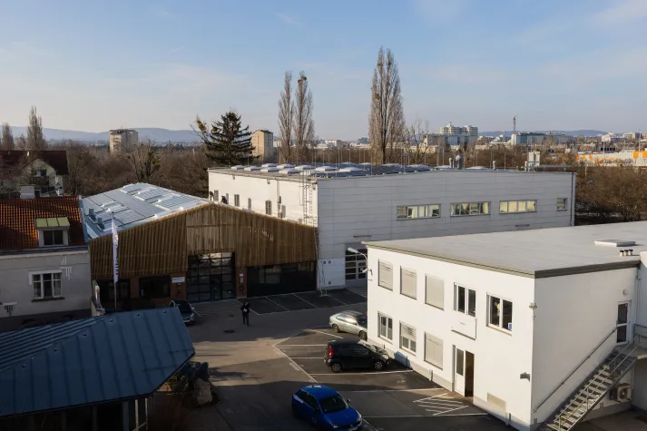 Firmengelände mit modernen Gebäuden, darunter ein Haus mit geneigtem Dach und Solardächern sowie ein weißes Gebäude mit Außentreppe