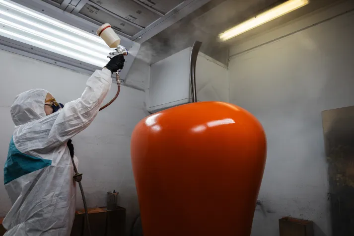 Person in Schutzanzug sprüht mit Farbpistole ein großes Apfelmodell an