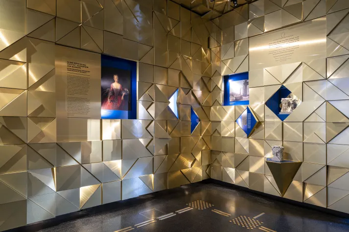 Ausstellungsraum: Opernhaus Bayreuth mit goldenen geometrischen Wänden, Vitrinen mit historischen Exponaten und einem Porträt.