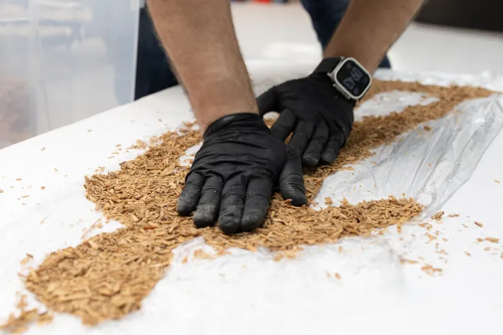 Detailaufnahme: Zwei Hände in schwarzen Handschuhen drücken Hanffasern in eine Negativform