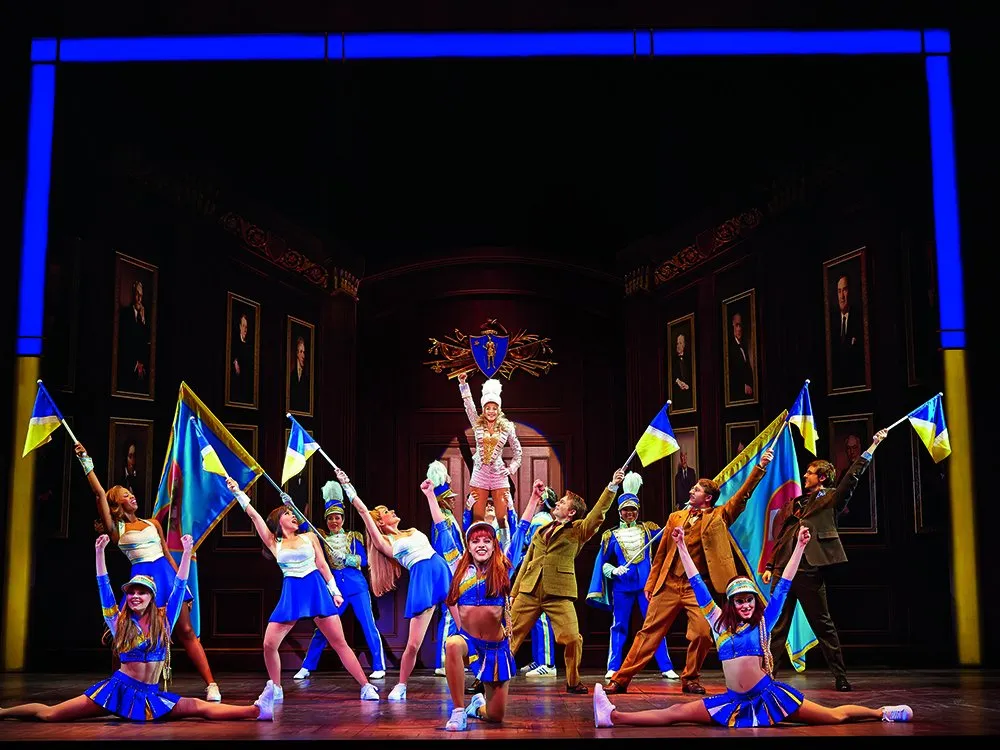 Szene: Gruppe and Cheerleadern in blau-gelben Kostümen und Pom-Poms