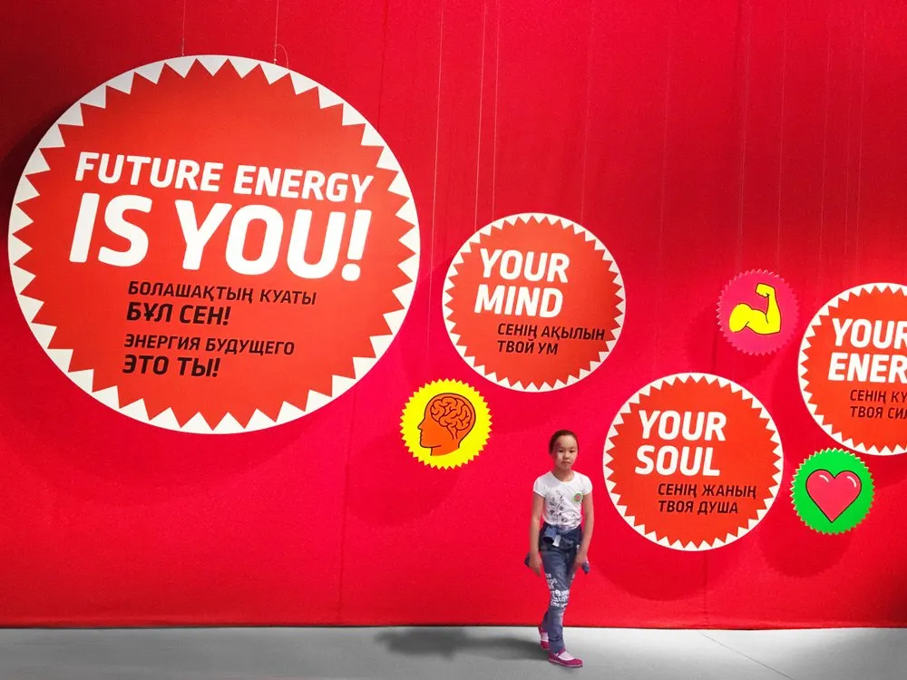 Roter Hintergrund mit Schildern "Future Energy is You!", Symbole (Herz, Muskel, Gehirn) und Texten