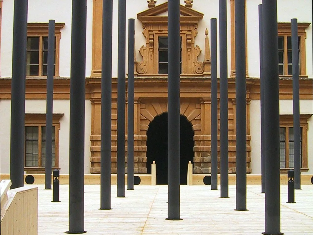 Vorplatz mit schwarzen Säulen vor einem Gebäude mit ornamentierter Fassade und Bogenportal