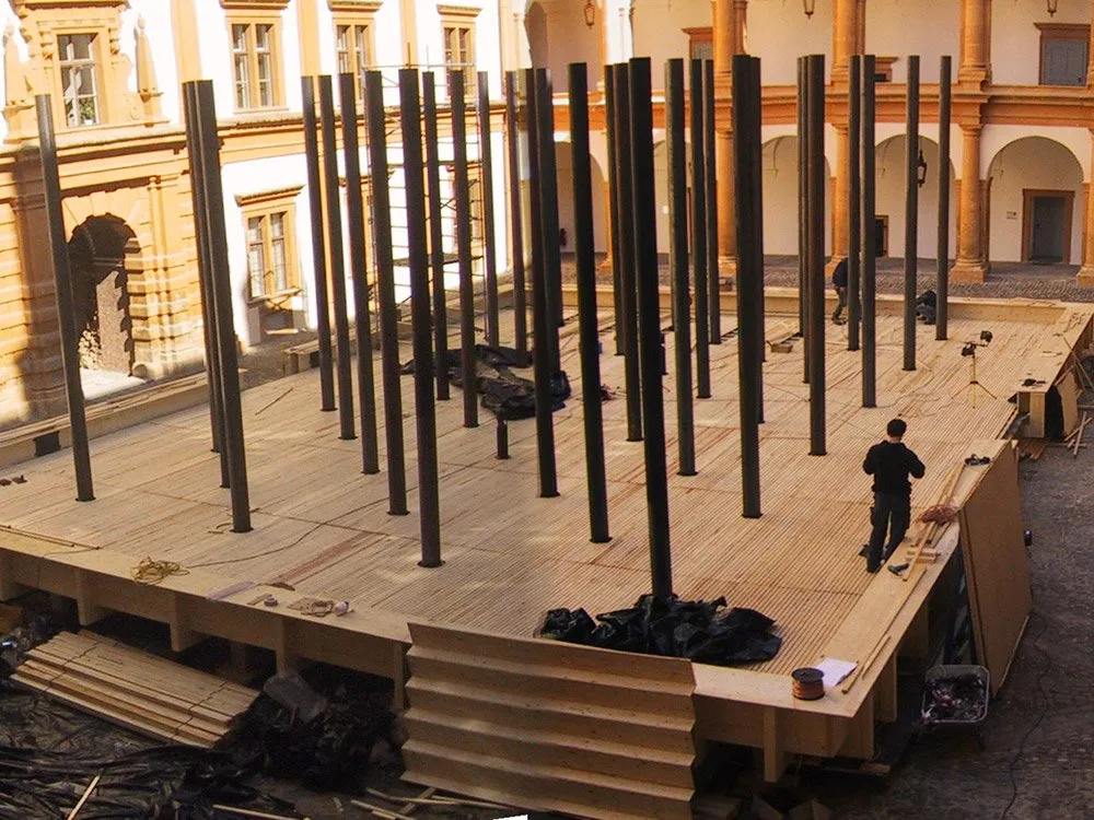 Holzpodest mit schwarzen Säulen im Innenhof eines Gebäudes mit historischer Fassade, Arbeiter bei der Einrichtung, Baustoffe ringsum