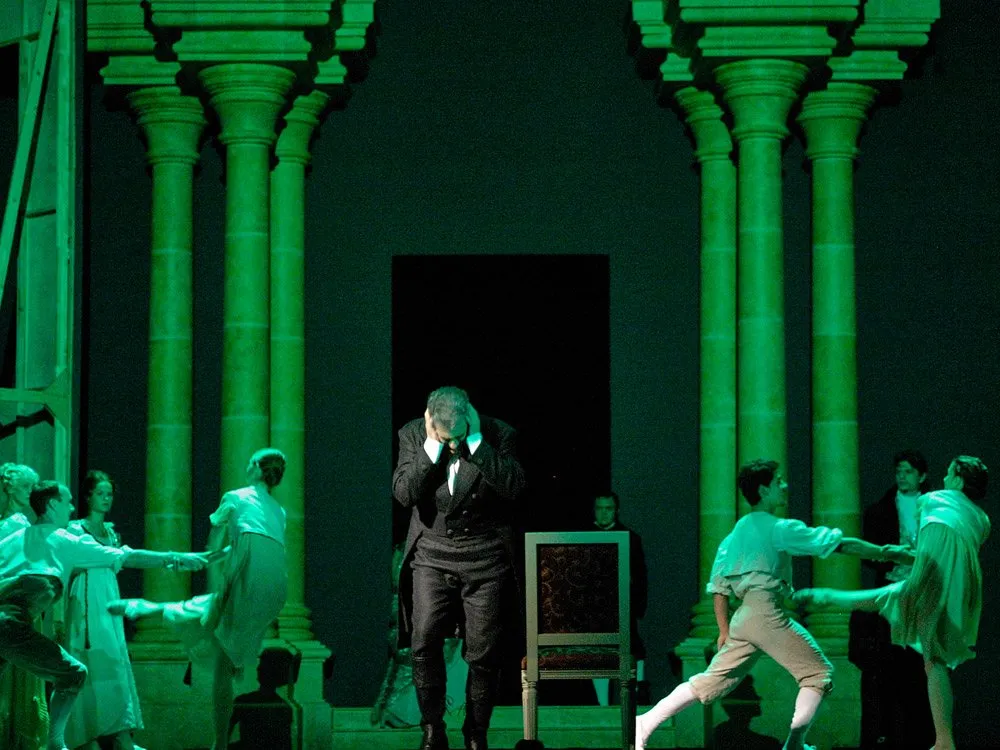 Mann in Schwarz, der sich den Kopf hält, umgeben von tanzenden Figuren, grün beleuchtet