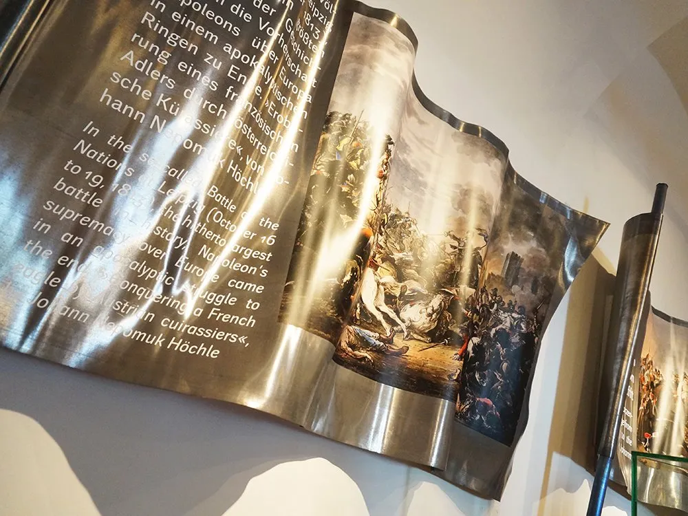 Detailansicht: Fahne aus Metall, gewellt geformt, mit Bildern und Text