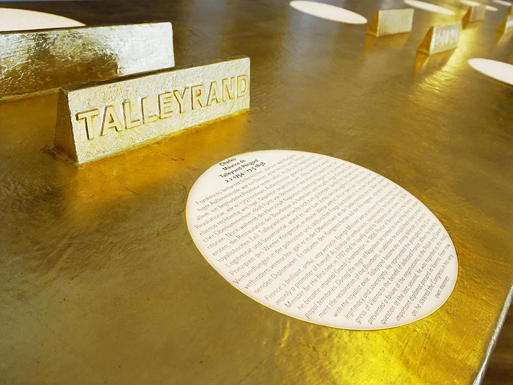 Detailansicht auf goldenen Tisch: Namensplakette "Talleyrand" mit Text auf Runder Scheibe