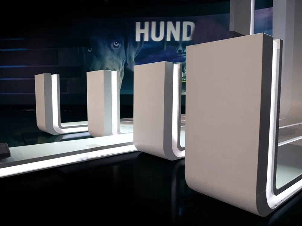 modernes Studio-Set mit weißen, U-förmigen Pulten und einer Projektionswand im Hintergrund