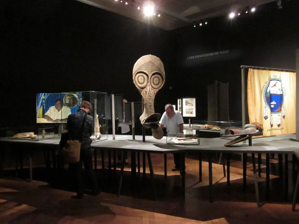 AUsstellungsraum: Zwei Besucher betrachten Artefakte und Infopaneele auf Tischen