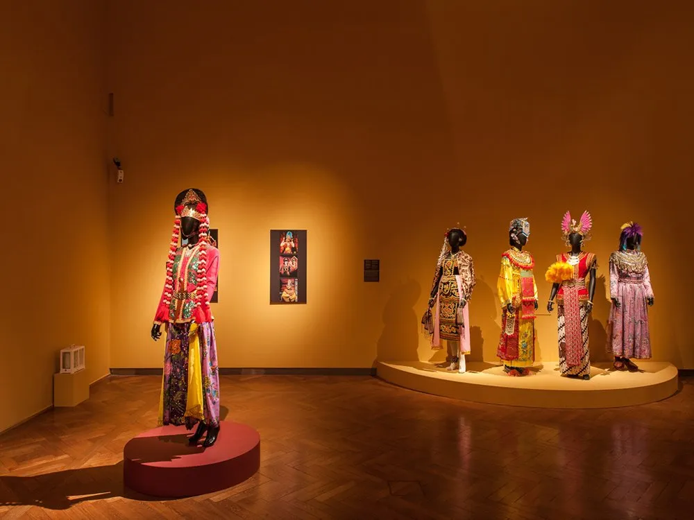 Ausstellungsraum: Mannequins mit bunten traditionellen Kostümen auf Podesten, ein Bild mit kulturellen Motiven an der Wand