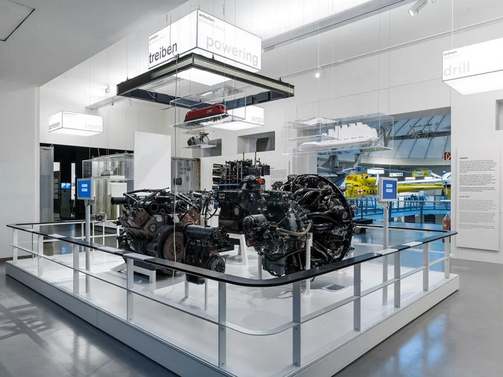 Ausstellungsraum: Weißer Raum mit einer Ausstellung von Motoren unter der Überschrift "treiben powering", umgeben von Informationspaneelen.