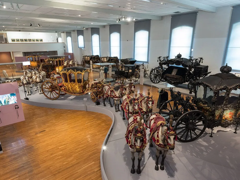 Ausstellungsraum: Verschiedene historische Kutschen, einige mit Pferden dekoriert, auf einer geschwungenen Plattform