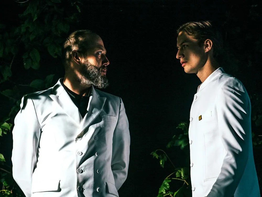 Szene: Zwei Schauspieler in weißen Anzügen stehen sich dramatischen gegenüber