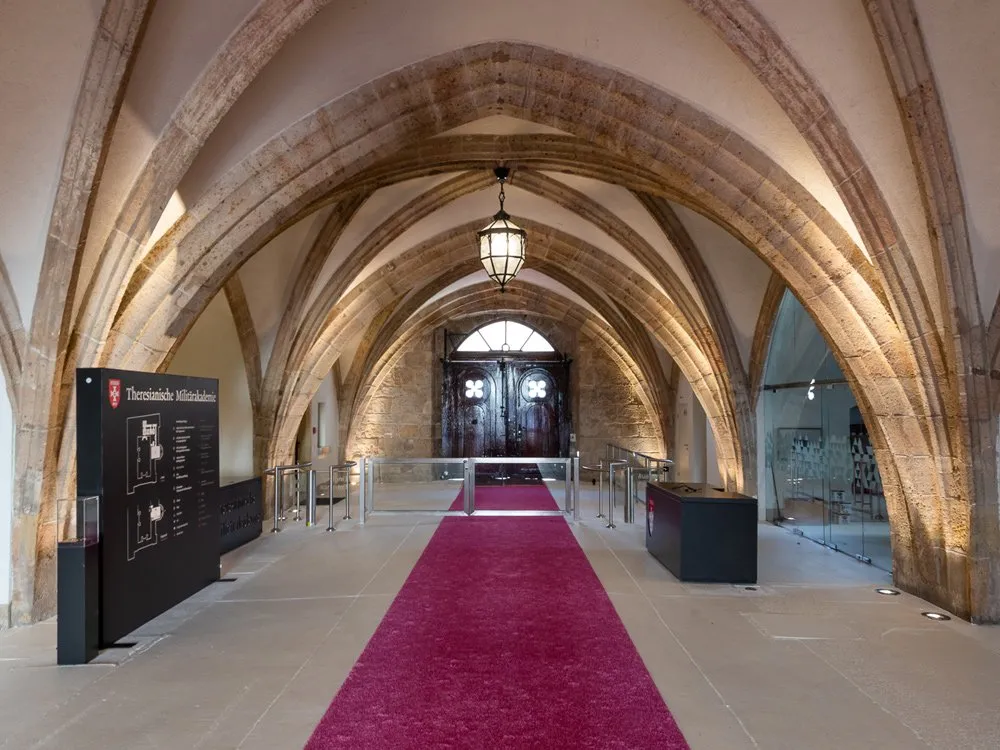 Raum mit gotischen Bögen, rotem Teppich und Informationspanel zur Theresianischen Militärakademie