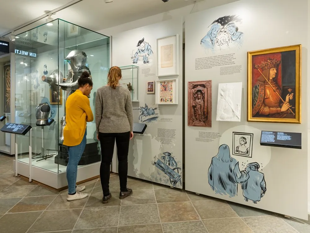 Ausstellungsraum: Vitrine mit einer Ritterrüstung und Artefakten, umgeben von Wandbildern und Gemälden 