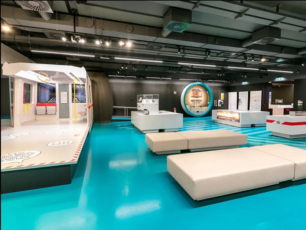 Ausstellung mit blauem Boden, Modell des X-Waggons, interaktiven Vitrinen und einem runden Display