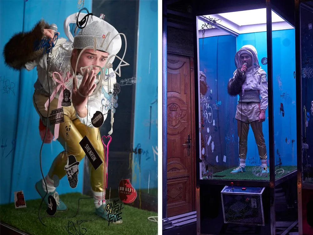 Zwei Personsn in Glasvitrinen umgeben von Graffiti und Stickern, eine mit goldener Hose und Mütze, die andere mit Astronautenanzug.