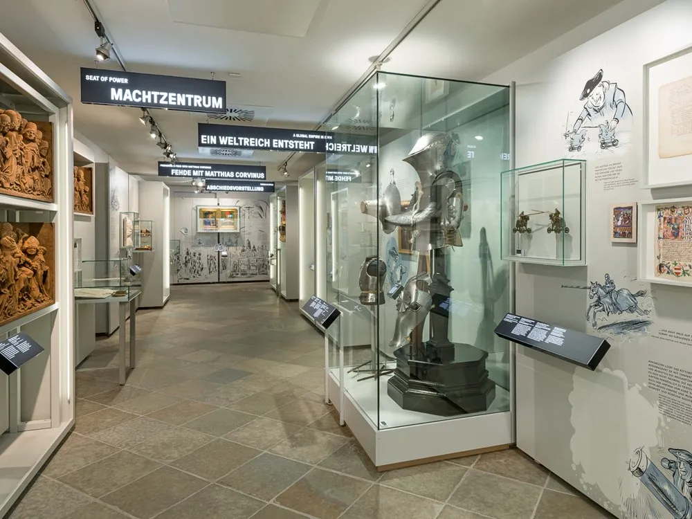 Ausstellungsraum: Vitrinen mit Artefakten, darunter eine Ritterrüstung und informativen Wandbildern