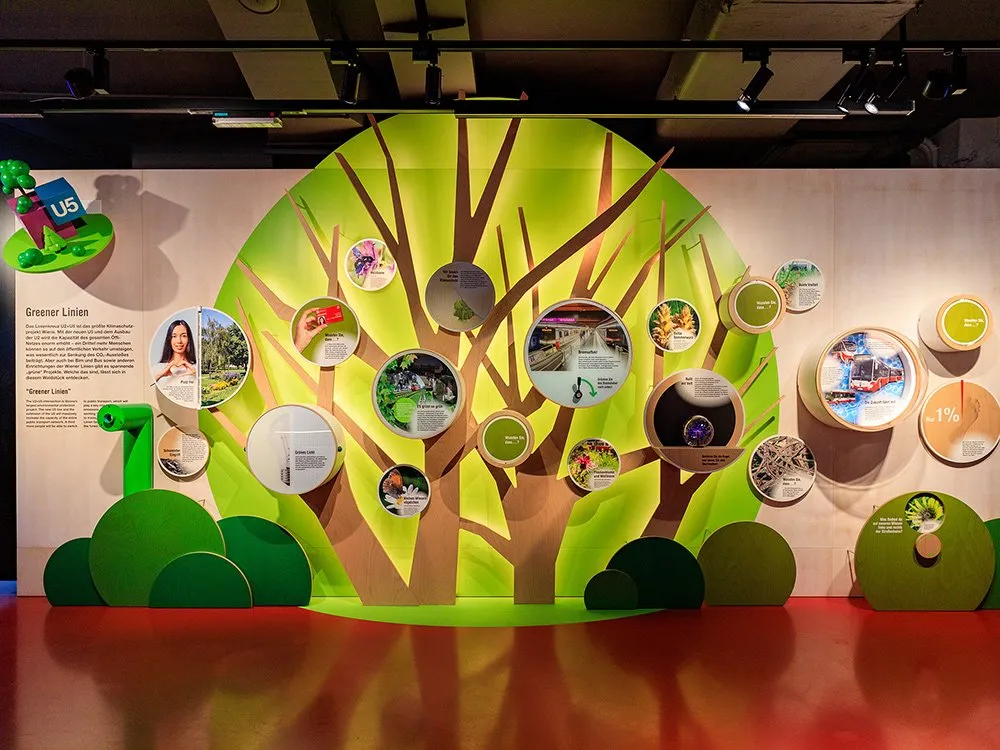 Ausstellungsbereich im Infocenter U2/U5 mit baumförmigem Display zu Klimaschutzprojekten der Wiener Linien, inkl. Photovoltaik, Blumenwiesen und Paketzustellung