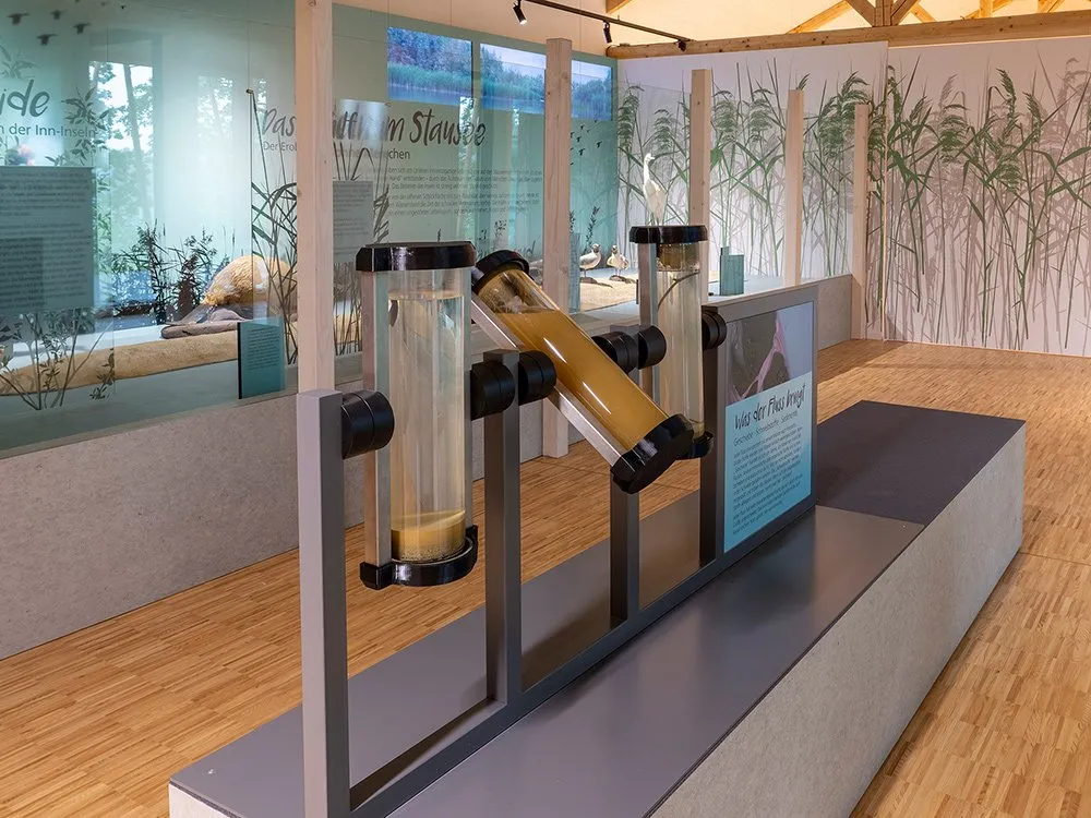 Detailansicht: Drei Glasröhren mit unterschiedlichen Bodenproben, gefüllt mit Schichten von Sand, Erde und organischen Materialien, auf einem Metallgestell