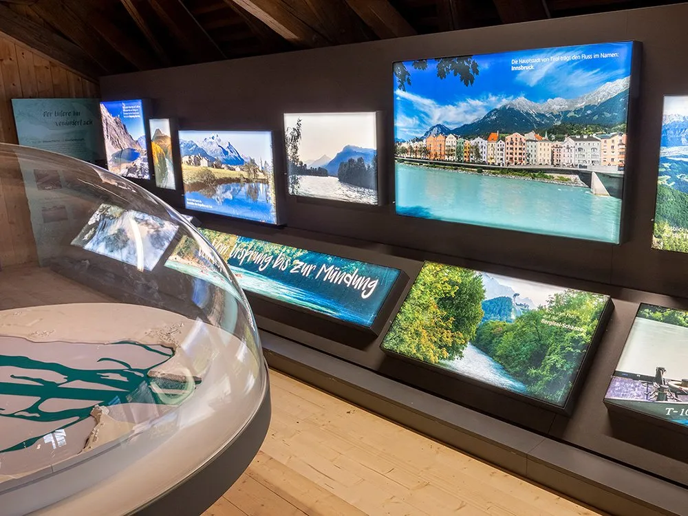 Bildschirme zeigen den Verlauf des Inns, Vogelzug und Auwälder im Europareservat Unterer Inn, mit Blick auf den Stausee und Schloss Frauenstein.