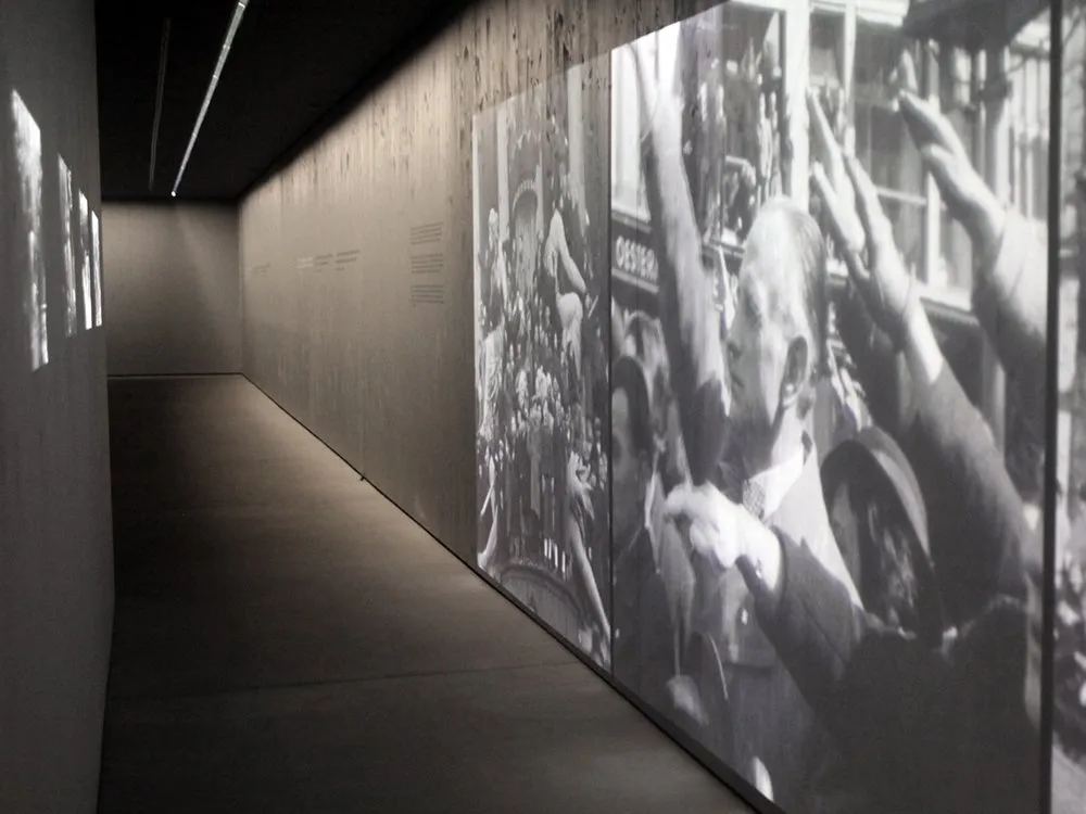 Schmaler, schwach beleuchteter Korridor mit projizierten Schwarz-Weiß-Fotos von Menschenmengen