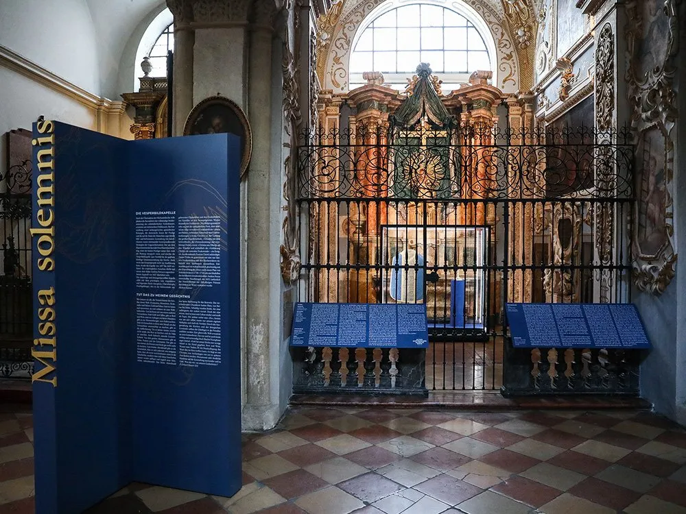 blaue Ausstellungstafel mit der Überschrift "Missa Solemnis" und Texten zur Vesperkapelle, vor einem barocken Altar