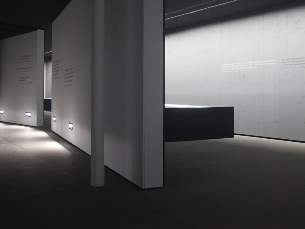 schmaler, schwach beleuchteter Ausstellungsraum mit projizierten Texten