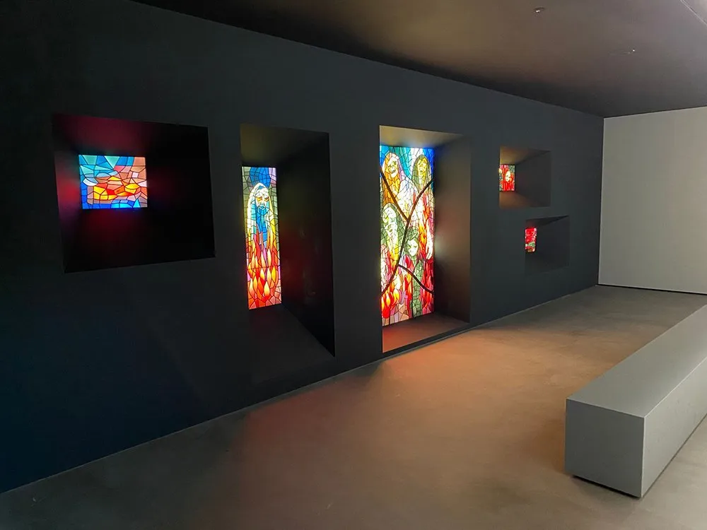 dunkler Ausstellungsraum mit eingelassenen Fenstern, die kirchliche Glasmalereien zeigen