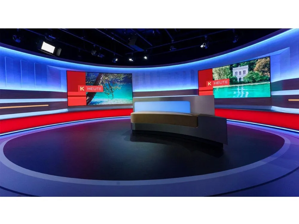 "Kärnten heute"-Studio mit gebogener Bühne, LED-Wänden mit Landschaftsbildern, roten Akzenten und einem zentralen Pult