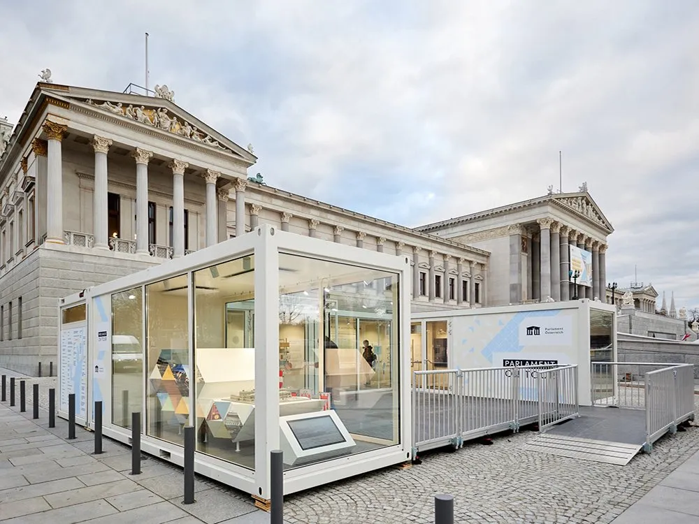 Weiße Container mit Glasfront vor dem Parlament