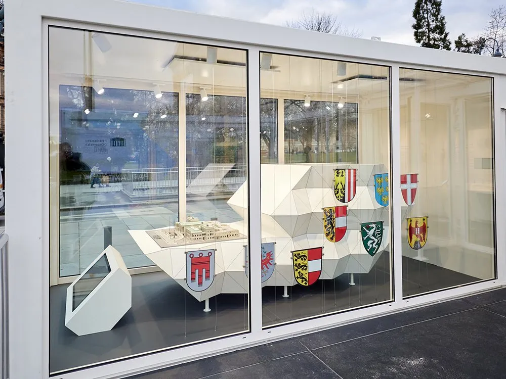 Weißer Container mit Glasfront, innen mit Modellen und Wappenschilder der Bundesländer