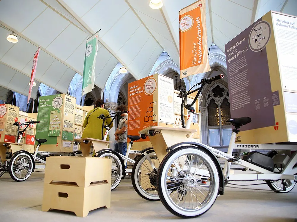 Frontalere Ansicht auf E-Lastenfahrräder, Besucher sehen sich die Plakate an.