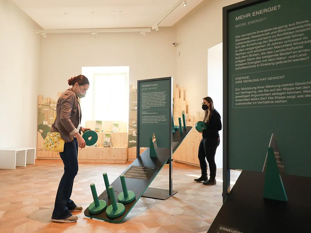 Zwei Personen interagieren mit einer interaktiven Station und Infotafeln