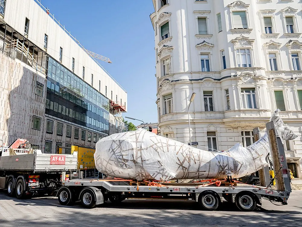 Der Praterwal „Poldi“ wird auf einem LKW vor dem Wien Museum transportiert, eingewickelt in Folie und gesichert mit Holz und Seilen.