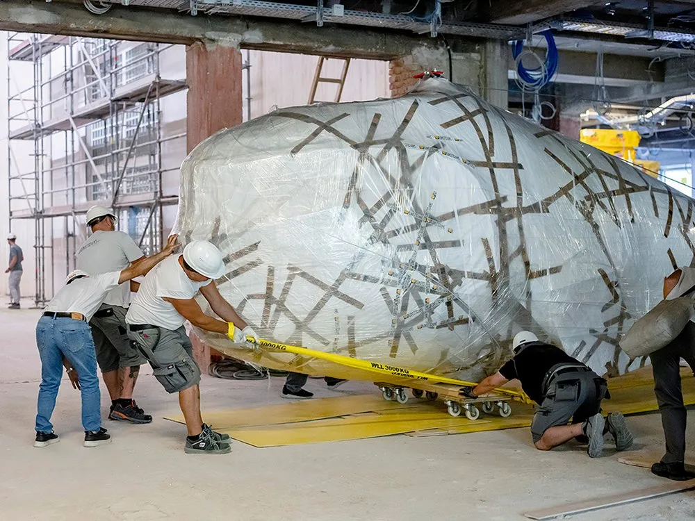 Arbeiter schieben den eingewickelten Praterwal „Poldi“ auf Rollen