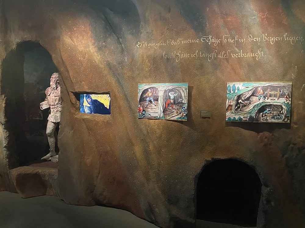 Höhlenkulisse mit einer historischen Skulptur, drei Gemälden und einem Text in gotischer Schrift