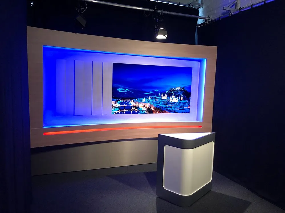 Kleines Studio  mit LED-Rückwand, die eine nächtliche Stadtlandschaft zeigt, und  modernen Sprecherpult.