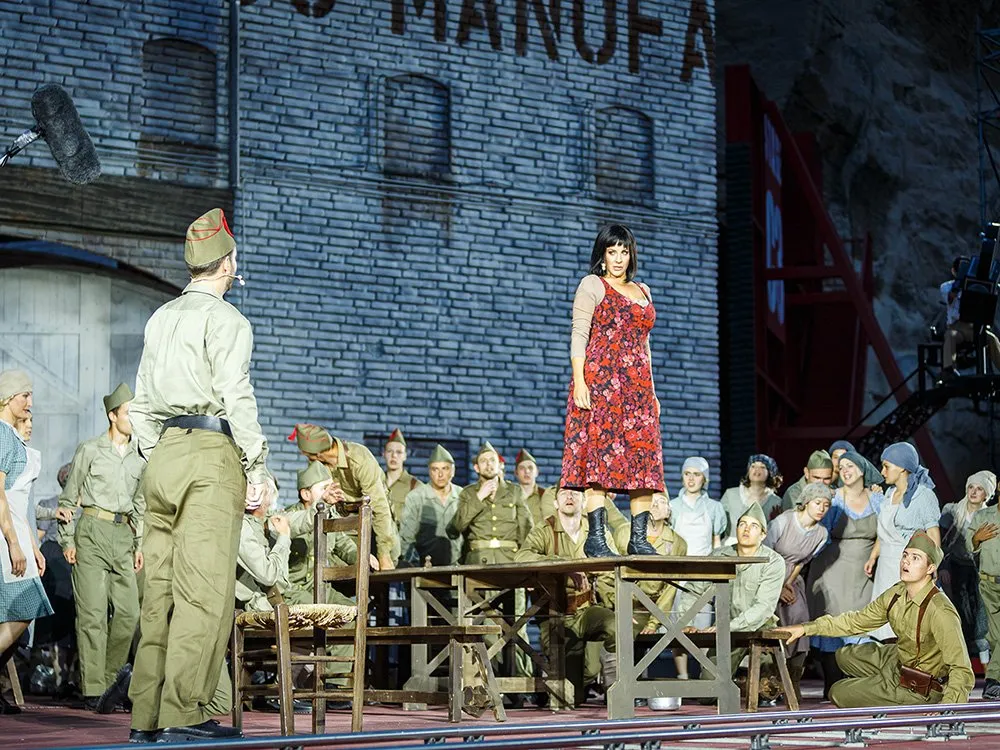 Frau in rotem Kleid steht auf einem Tisch umgeben von einer Gruppe Soldaten