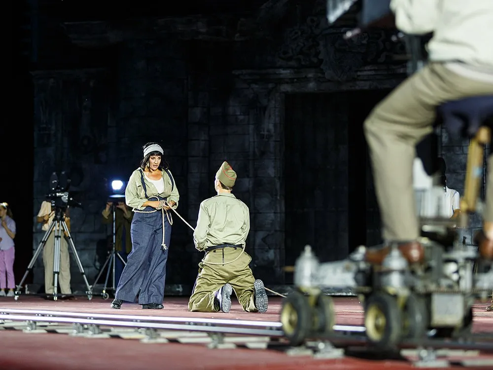 Szene: Frau in blauem Outfit, die einen geknieten Soldaten mit einem Seil festhält